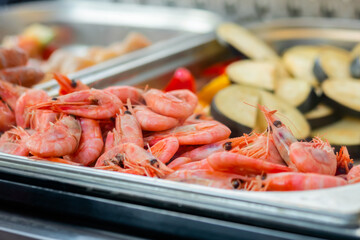 Cooked fresh red shrimps, zucchini in restaurant food container at summer local market - close up. Outdoor cooking, gastronomy, seafood, takeaway, street food concept