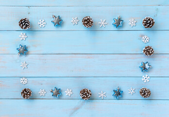 Christmas border decoration on light blue wooden background. Blue and silver stars, snowflakes, snow covered cones. Flat lay, copy-space.