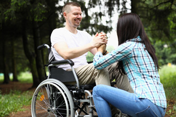 Disabled man in love sit in wheelchair and hold woman hands in park.