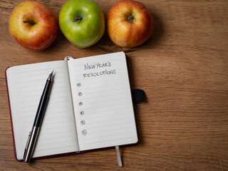 Notebook with New Year's resolutions surrounded by apples and a fountain pen