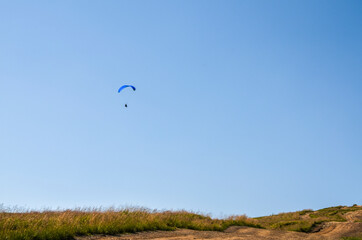 Paraglider flying over the mountains against the blue sky in clear weather. Extreme sport, lifestyle and freedom concept