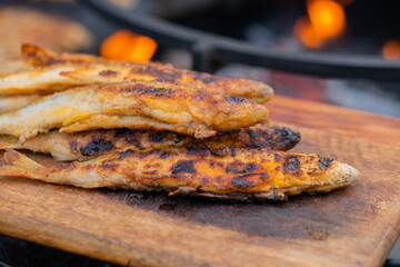Crispy breaded european smelt fish on wooden cutting board at summer outdoor food market: close up. Seafood, barbecue, gastronomy, cookery, street food concept