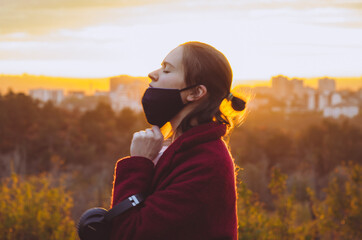 Fototapeta premium Side view of young woman taking the face mask off for a gulp of fresh air backlit by orange sunset light. Concept: breathing, safety, freedom, covid pandemic