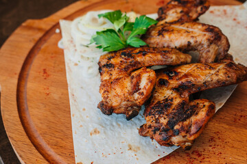 Fried chicken wings with herbs lie on a flat cake. Meat on a wooden board.
