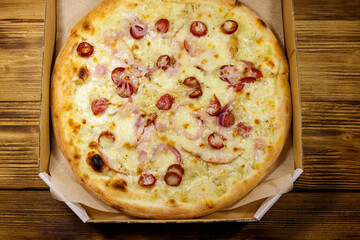 Delicious fresh pizza in cardboard box on a wooden table. Top view. Concept for home delivery of food, fast food, delivery of pizza