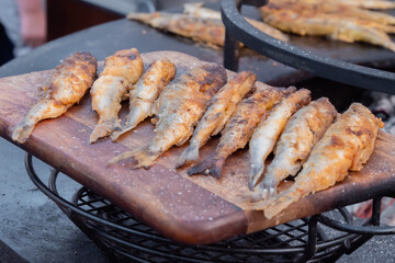 Crispy breaded european smelt fish on wooden cutting board at summer outdoor food market: close up. Seafood, barbecue, gastronomy, cookery, street food concept