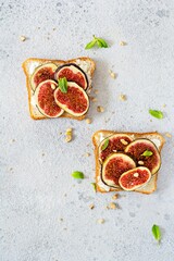 Crispy bruschetta with soft ricotta, ripe figs, walnuts and pine nuts, mint and honey on a light background. Figs fruit toast on marble table with honey and walnut. Top View.