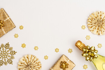 Festive white background with gold decoration , bottle of sparkling wine and gift box, paper christmas tree decorations and glittering snowflakes , flat lay, top view, copy space