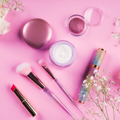 Obraz na płótnie Canvas Shiny make up products and accessories on pink background with flowers. Trendy holographic brushes.