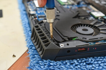 repairing vent part of gaming laptop and fitting screw with mini screwdriver on blue table cloth...