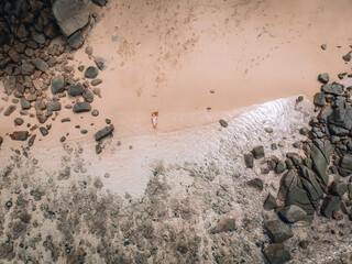 sexy caucasian woman on the beach on the sand near the waves and stones. Beautiful woman covers her naked breasts with her hands. Phuket. Thailand. Aerial top view.