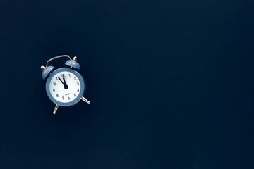 Blue vintage alarm clock shows 12 o'clock isolated on dark background. Wake up and hurry up. Hot...