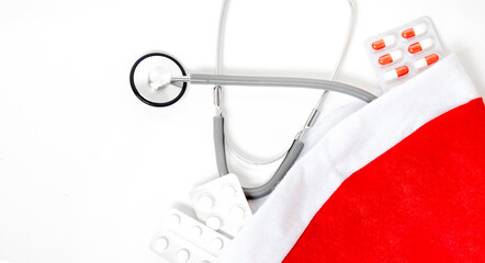 Medicine christmas new year concept banner during coronavirus covid-19 time. Top view of medical pills, disposable protective face mask, gift box, stethoscope in santa hat on red background.