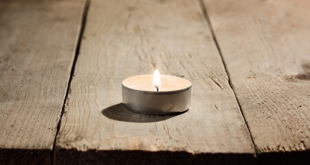 Obraz na płótnie Canvas Lonely small lighted burning round candle on a wooden background of rough untreated pine boards. Macro photography with great depth of field