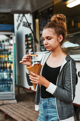Teenage girl eating potato fries from carton cone standing in front of food truck. Teenager having a fast food meal outdoors during summer vacations