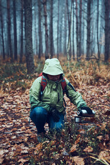 Woman with backpack having break during autumn trip on autumn cold day pouring a hot drink from thermos flask. Active middle age woman wandering around a forest actively spending time