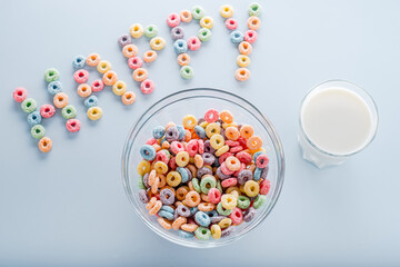 Colored fruit grain loops in a bowl, a glass of milk. word with grain loops happy on a blue background. The concept of a positive breakfast.