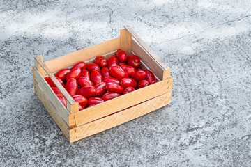 Juicy and fresh tomatoes in wooden box on old cracked concrete background. Top view with text space.