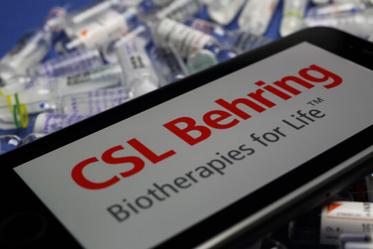 Viersen, Germany - May 9. 2020: Close up of mobile phone screen with logo lettering of CSL Behring biotherapies pharmaceutical company on pile drug ampules