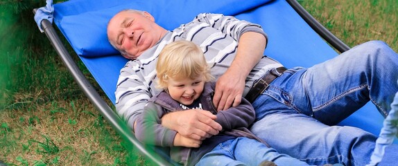 Grandfather and grandson resting in a garden hammock, swing. Family, leisure, relax, summer vacation banner.