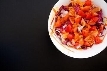 Salad with carrots and tomatoes on black table, top view
