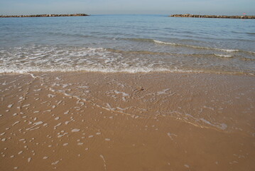The wave runs over the beach sand.
Winter sunny day on the mediterranean sea. Small waves are splashing along the coast. A small wave of clear water rolls onto the shore with foam. Sea water stretches