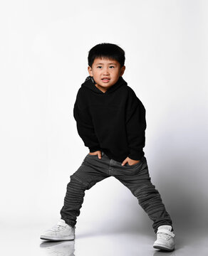 Cool Korean little boy in a stylish black sweatshirt with a hood and jeans posing in the studio on a white background and. New collection of comfortable children's clothing.