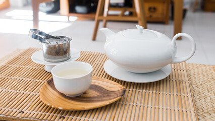 Tea set on a bambou tray. Porcelain teapot and teacup, fresh organic green tea leaves in a metal filter. Beautiful professional shot of the teaware. Morning breakfast.