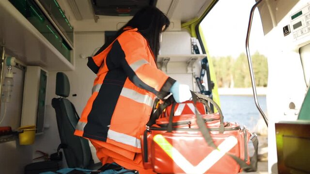 Young female paramedic grabs huge equipment bag and leaves emergency vehicle