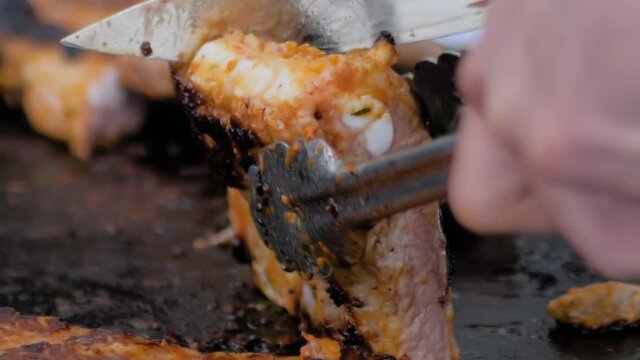 Slow motion: chef holding knife, cutting prepared juicy meat steaks on brazier at summer local food market - close up view. Outdoor cooking, gastronomy, cookery, street food concept