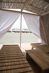 Little resting hut interior with white curtain and wooden benches at sandy beach.
