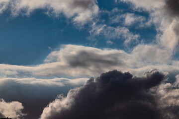 black cloud at the bottom of the image, while in the background white clouds shaded with gray float gently under a clear blue sky.