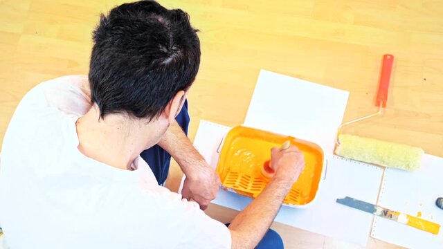 Painter Man At Work Stirring A Pot Of Orange Paint With A Brush To Make Reforms. Set Of Tools Of A Painter, Top View. 4k Stock Video Of Professional Painting Services, Rear View Of Contractor.