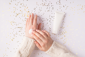 Using moisturizing cream on winter season concept.  Top flatlay overhead above close up view photo of female girl hands smearing white smooth cream on shiny background