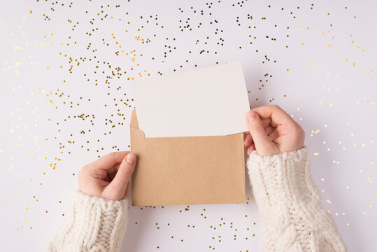 Top above close up overhead view photo of female hands holding kraft paper envelope with mock up copy space card inside over shiny golden background table
