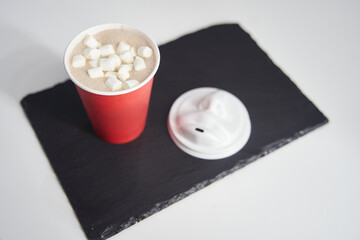 Red paper cup of coffee with marshmallows on a black tray.