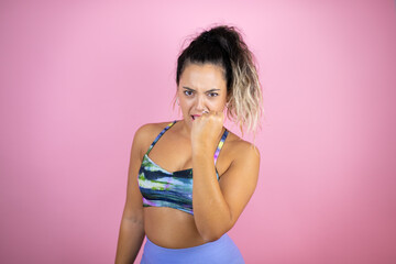 Young beautiful woman wearing sportswear over isolated pink background angry and mad raising fist frustrated and furious while shouting with anger. Rage and aggressive concept.