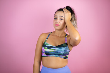 Young beautiful woman wearing sportswear over isolated pink background putting one hand on her head...