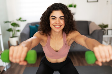 Attractive young woman squatting with two small weights at home