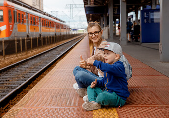 Woman with son on the platform near the train. Girl with a preschool boy sitting at the train station near the train. Travel by rail. Mother and son waiting for the train. Family trip. Bydgoszcz.