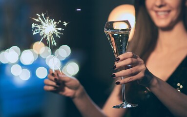 Woman celebrating New Year, toasting with champagne, holding sparkler or bengal light.
