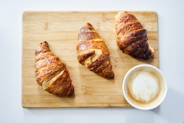 Golden fresh croissants with coffee on a wooden tray close up