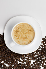 White clean background from above with a cup and saucer filled with coffee and half sprinkled with coffee beans.