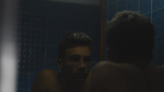 Portrait of young man or sad teenager in the bathroom looking at himself without doing anything - millennial reflexing 
