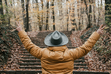 Woman in the woods during autumn making a peace hand sign with her back to the camera