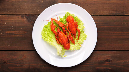 Steamed boiled crawfish on a lettuce leaf are ready to eat on a white plate on a wooden background. Copy space.