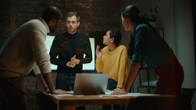 Diverse Multiethnic Team are Having a Conversation in a Meeting Room Behind Glass Walls in a Creative Office. Colleagues Lean On a Conference Table and Discuss Business, App User Interface and Design.