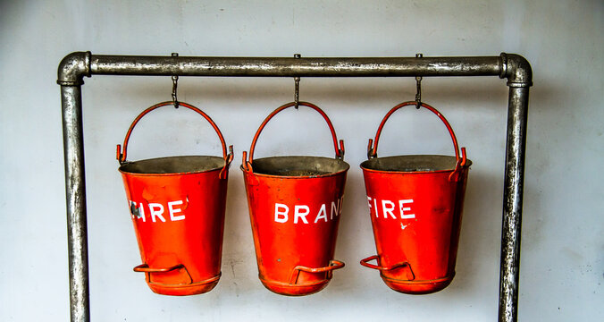 Closeup of three red old fire buckets hanging from a metal pipe