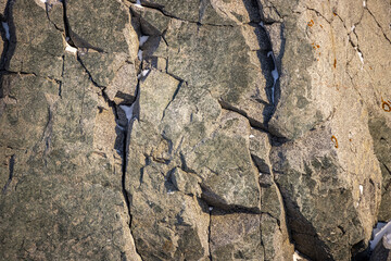 Rock texture. Snow and cracks on the surface of the cliff. Natural stone background.