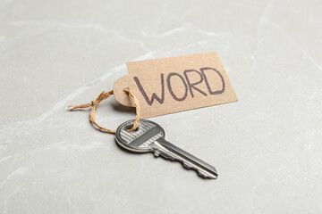 Metal key with tag on light grey table. Keyword concept